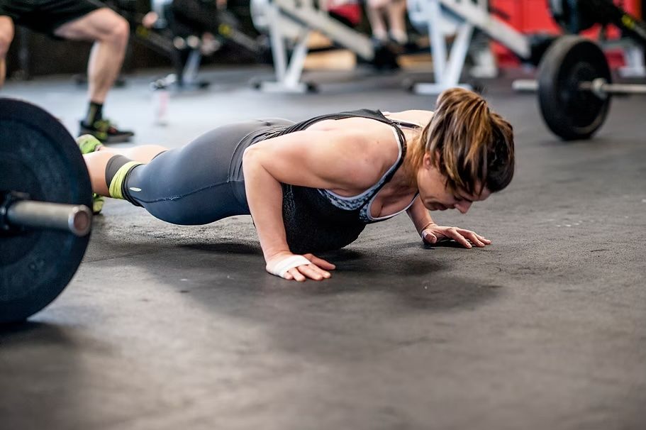 Woman doing push-ups on gym floor, arms extended, near a barbell.