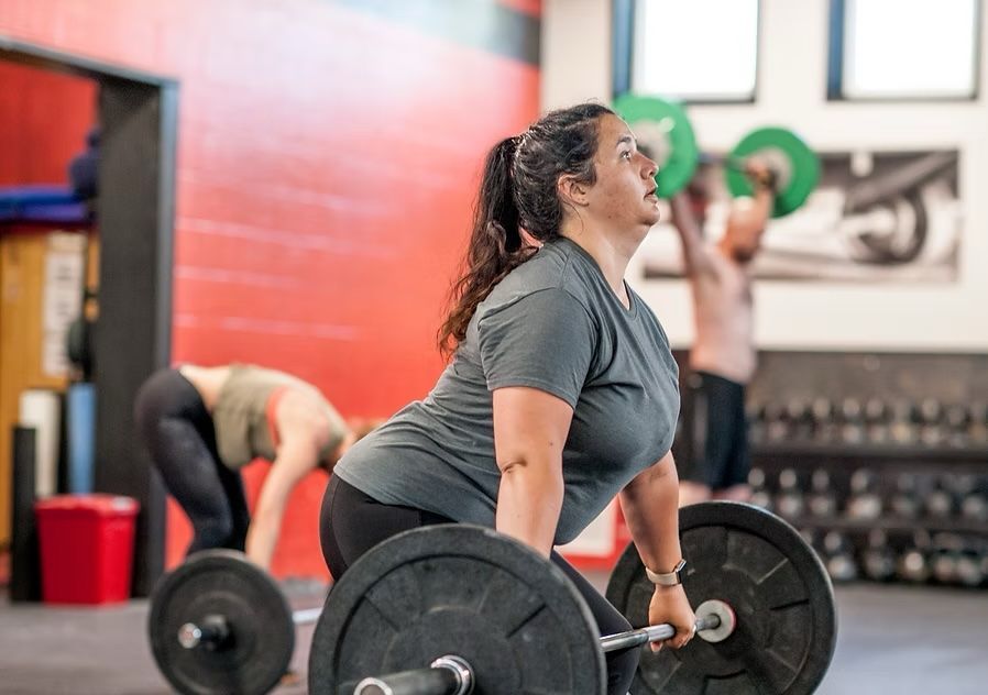 Woman performing a deadlift at a gym; others work out in the background.