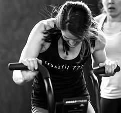 Woman intensely exercises on an Assault AirBike, wearing a tank top at a gym.