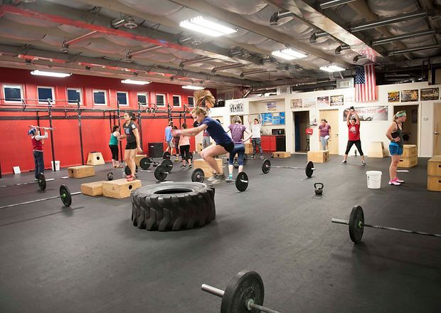 People working out in a gym, with weights, boxes, tires, and pull-up bars.