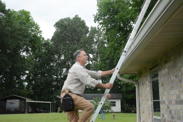 Man climbing a ladder to reach a gutter on a house, outdoors.