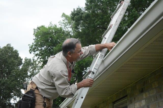 Man on ladder cleaning a gutter on a house.