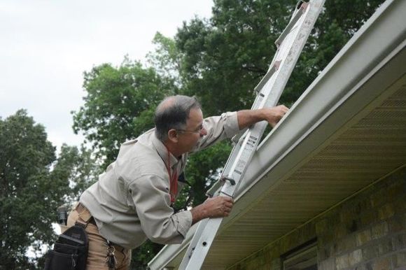 Man on ladder cleaning a gutter on a house.
