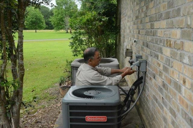 Man working on electrical panel near AC units, brick wall background, green lawn.