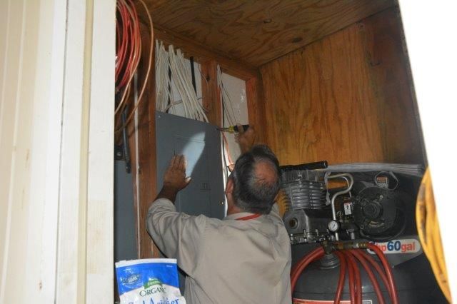 Man working on electrical panel in a wooden room, with compressor in the background.