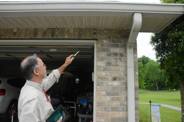 Man inspecting eaves of a garage with a pen. He's outside, pointing upwards at the beige siding.