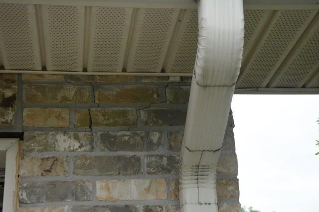Stone wall with crack below a white gutter and perforated soffit.