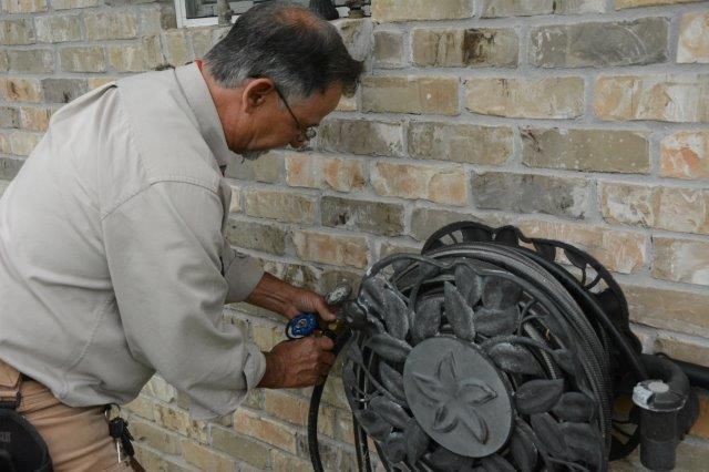 Man attaching a garden hose to a decorative reel mounted on a brick wall.