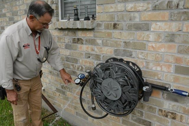 Man points at a hose reel attached to a brick wall.