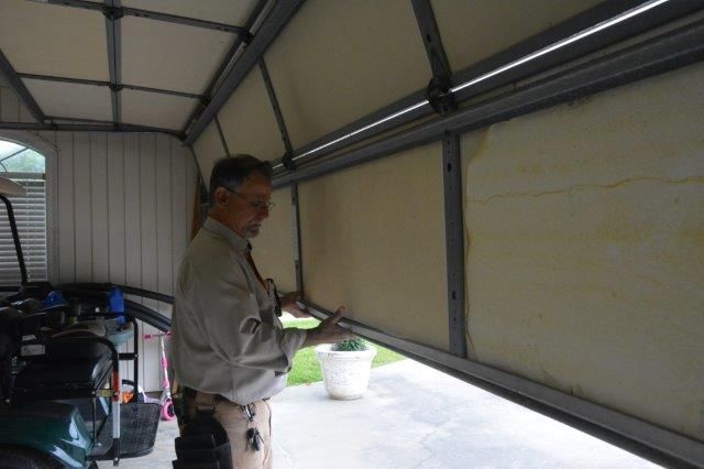 Man inspects garage door. Inside garage, door partially open; light tan insulation visible.