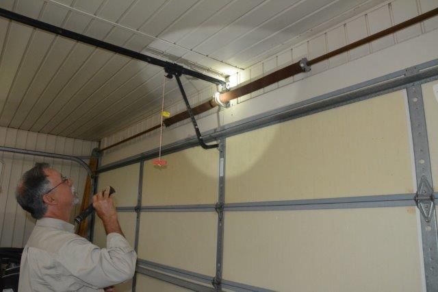 Man inspecting garage door with a flashlight, looking at a torsion spring.