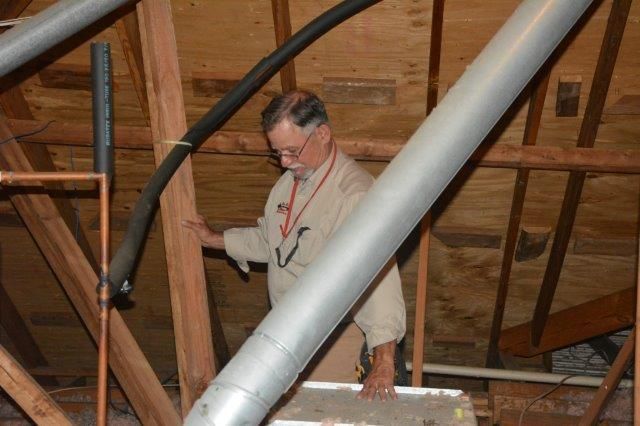Man in an attic inspecting pipes and ductwork.