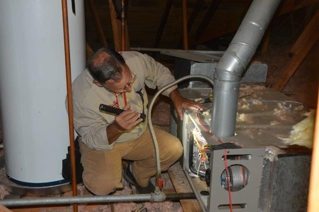 Man inspecting furnace in attic, using a flashlight.