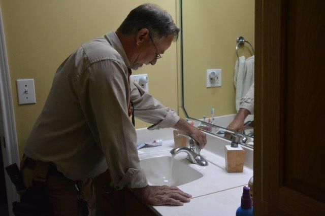 Man in bathroom washing hands at a sink. The man is reflected in the mirror.