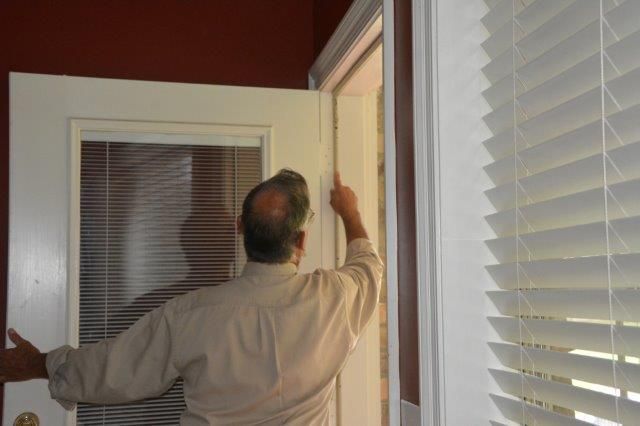 Man adjusting a white door frame. Blinds and a partially visible window are to the right. Red walls.