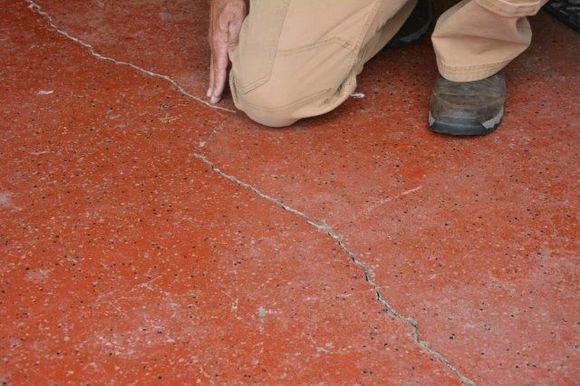 Person inspecting a long crack in a red concrete floor.
