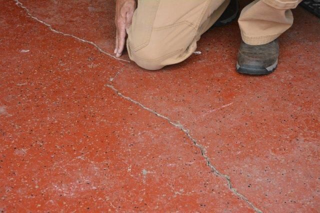 Person kneeling, touching a crack in a red concrete floor.