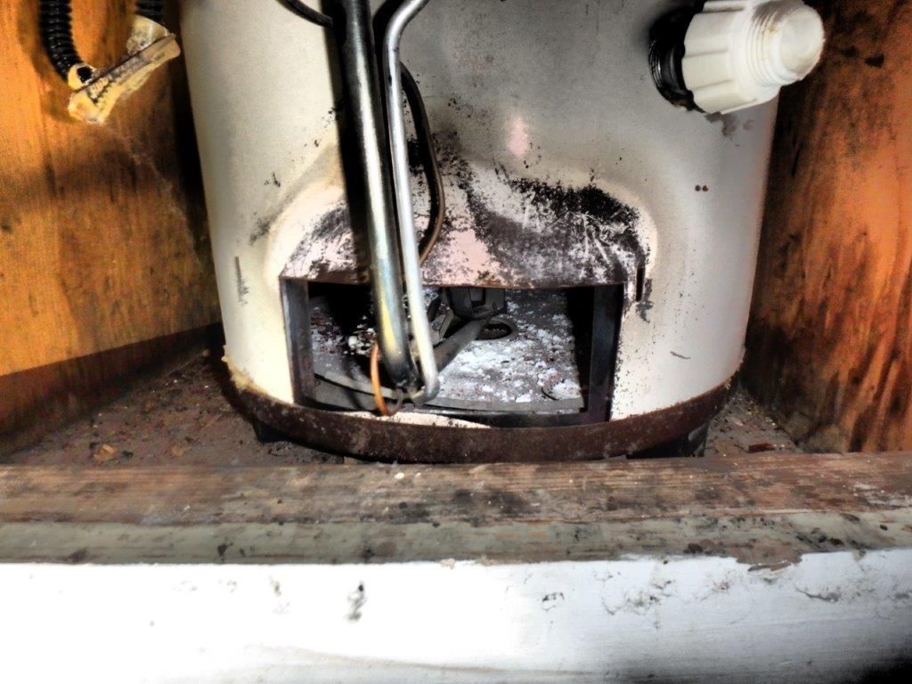 Gas water heater with a damaged burner area, showing soot and residue.