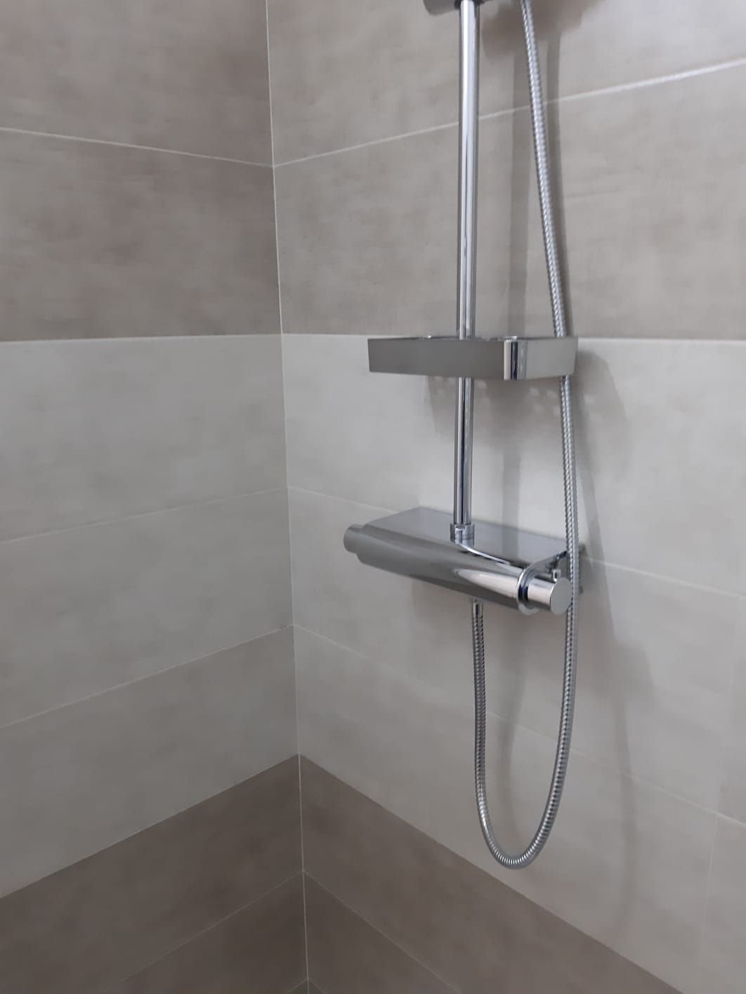 Un soffione della doccia con una mensola attaccata in un bagno.