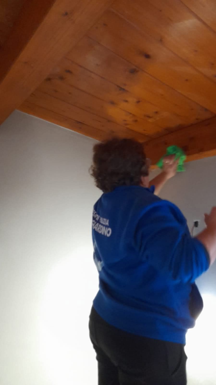 Una donna con una felpa blu sta pulendo il soffitto di una stanza.
