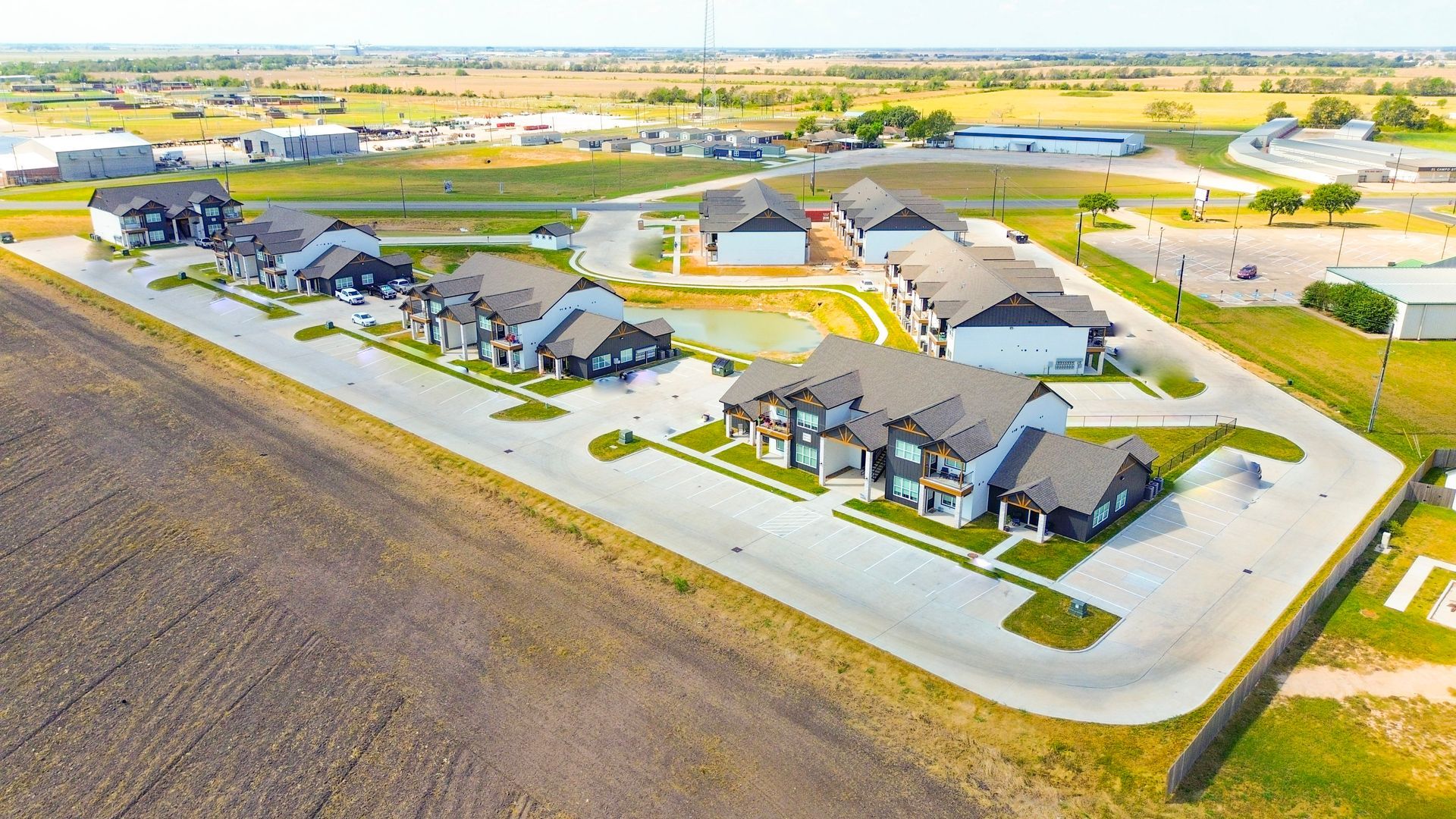 Aerial view of modern townhomes with light-colored siding, dark roofs, and manicured landscaping in a rural setting.