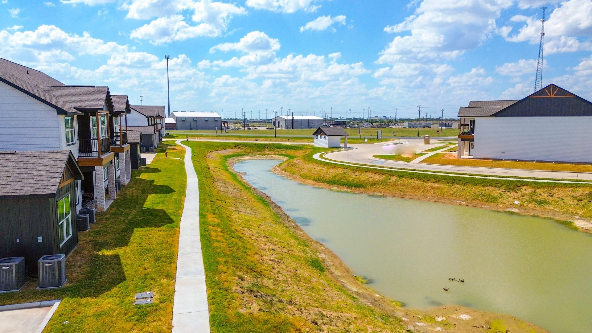 Row of townhomes next to a canal with a walking path, under a blue sky.
