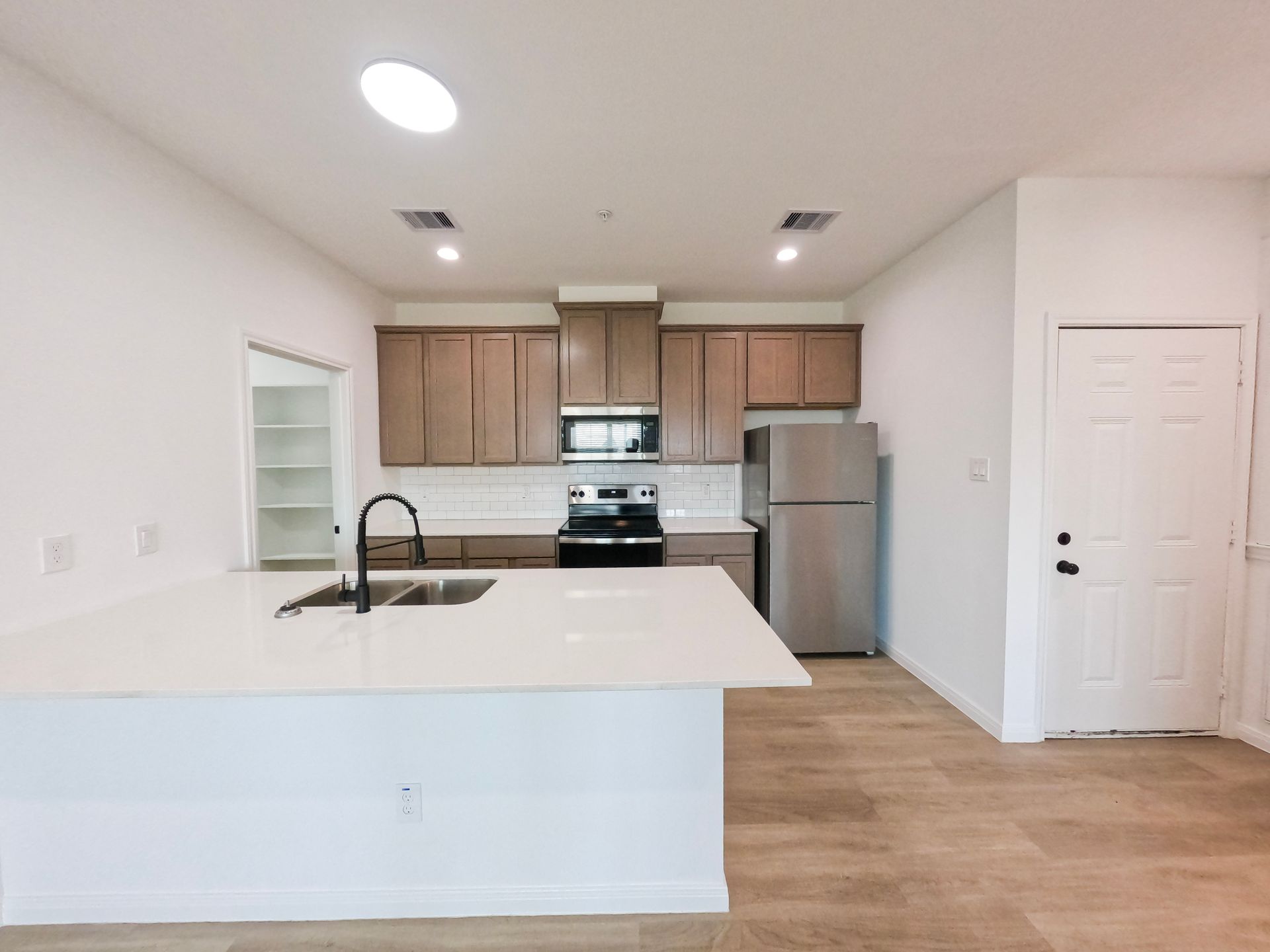 Modern kitchen with light wood cabinets, white countertops, and stainless steel appliances.