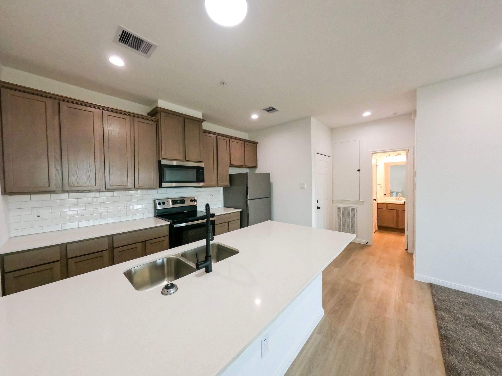 Modern kitchen with white countertops, brown cabinets, stainless steel appliances, and a view into a bathroom.