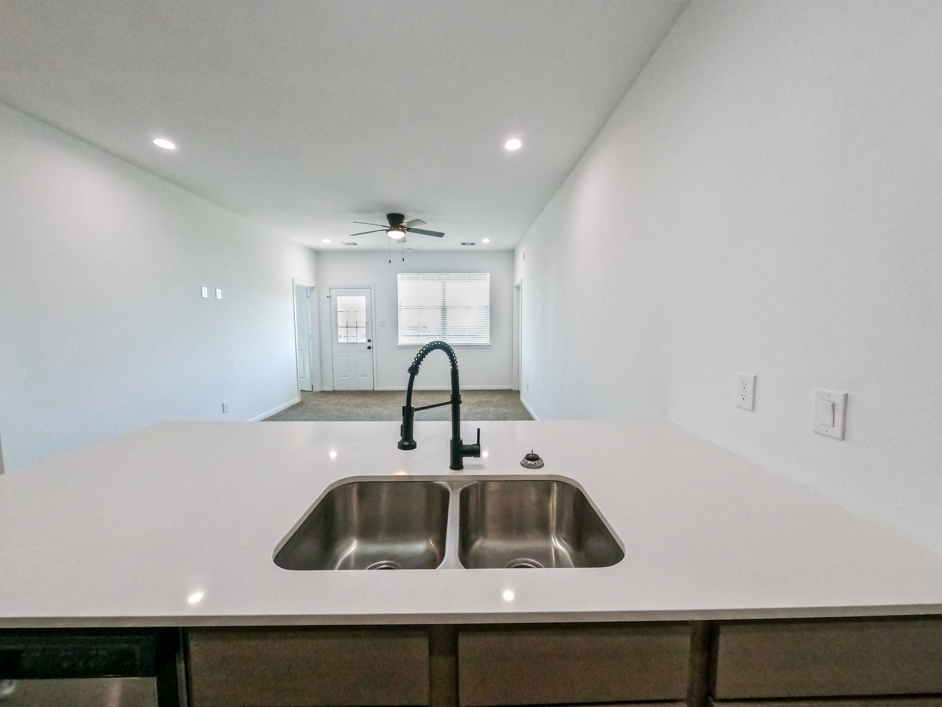 Kitchen sink and counter, with a view through a doorway into another room with a window.