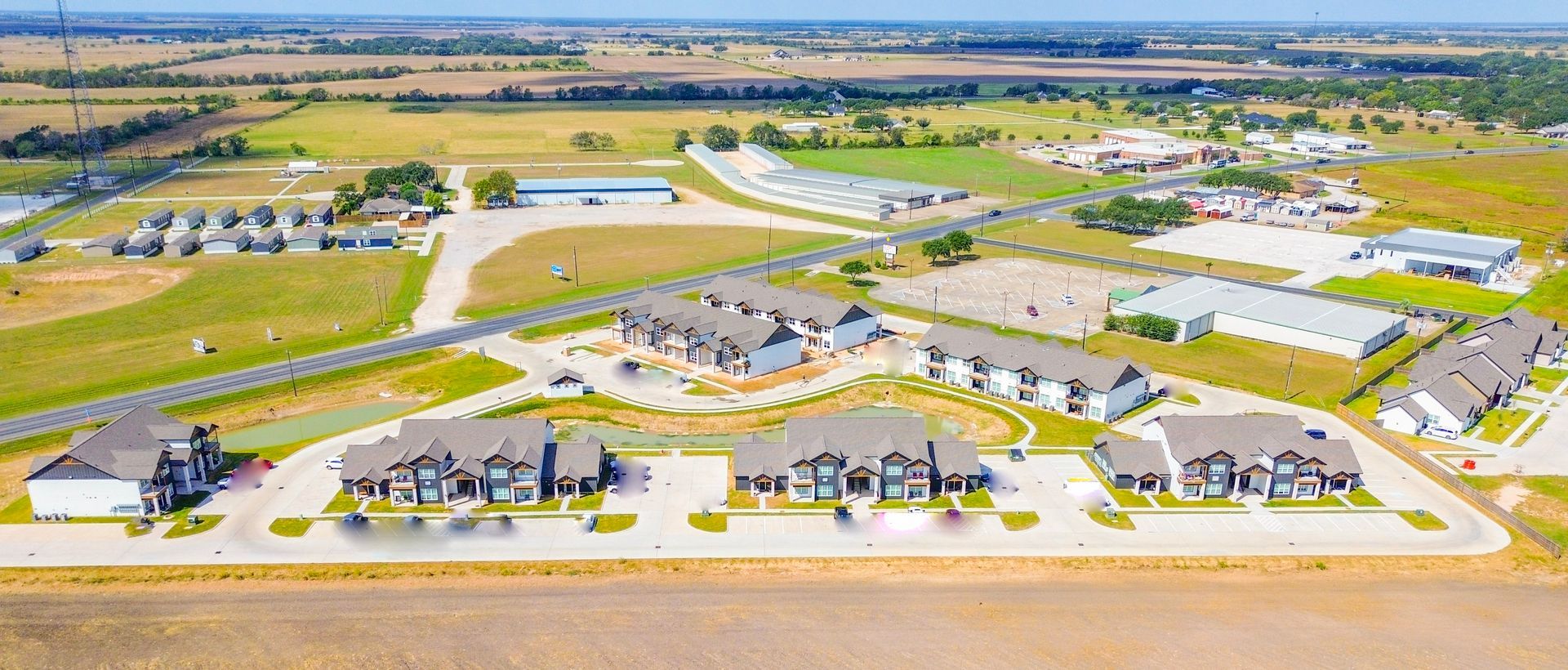 Aerial view of buildings, roads, and green fields under a blue sky.