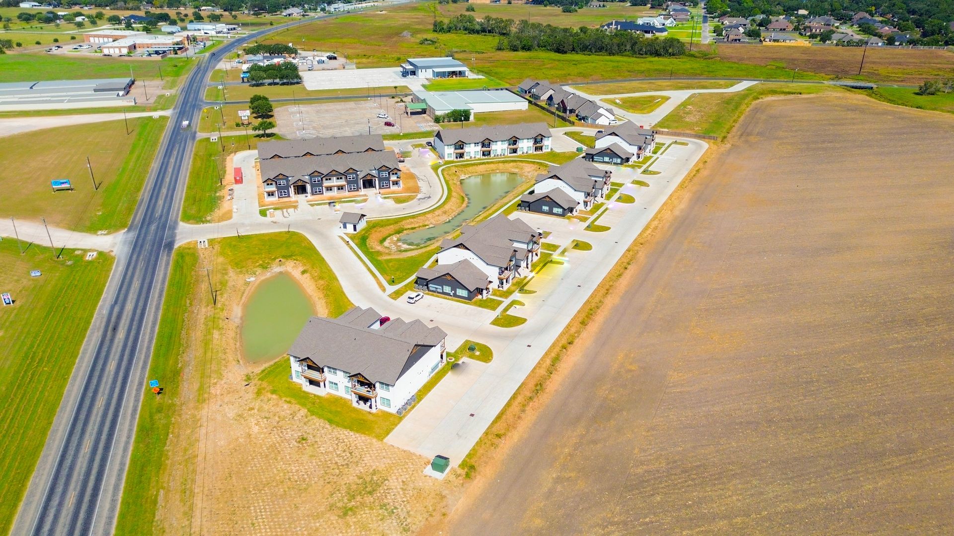Aerial view of apartment buildings with brown roofs near a road and field.