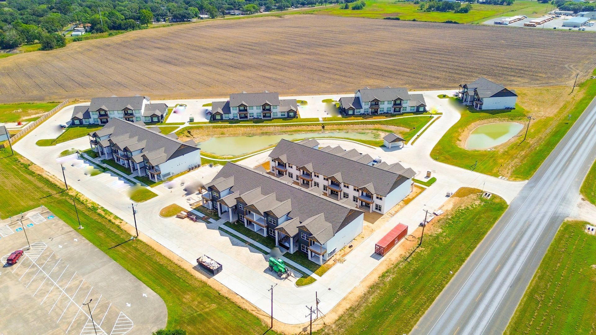 Aerial view of new apartment complex with brown roofs and a pond near a highway.
