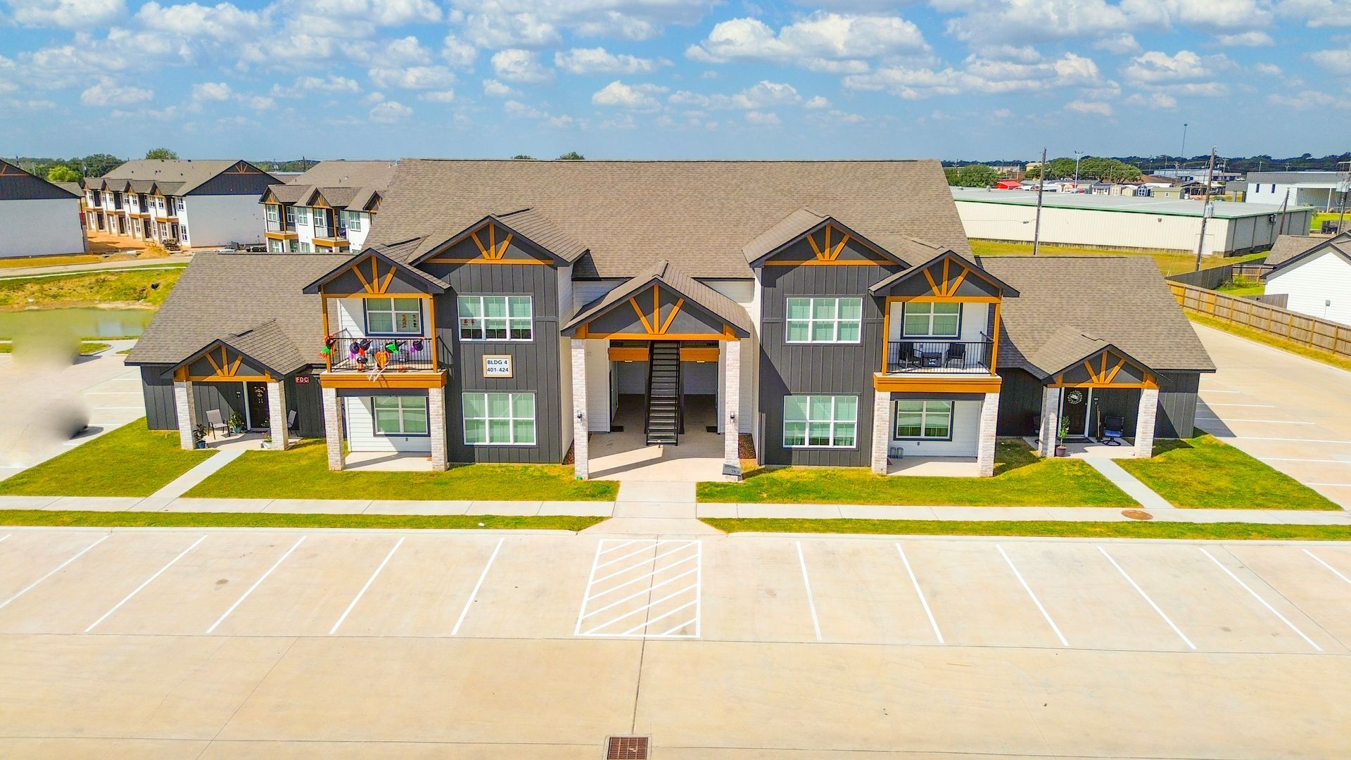 Apartment building with gray siding, brown roof, and parking lot on a sunny day.