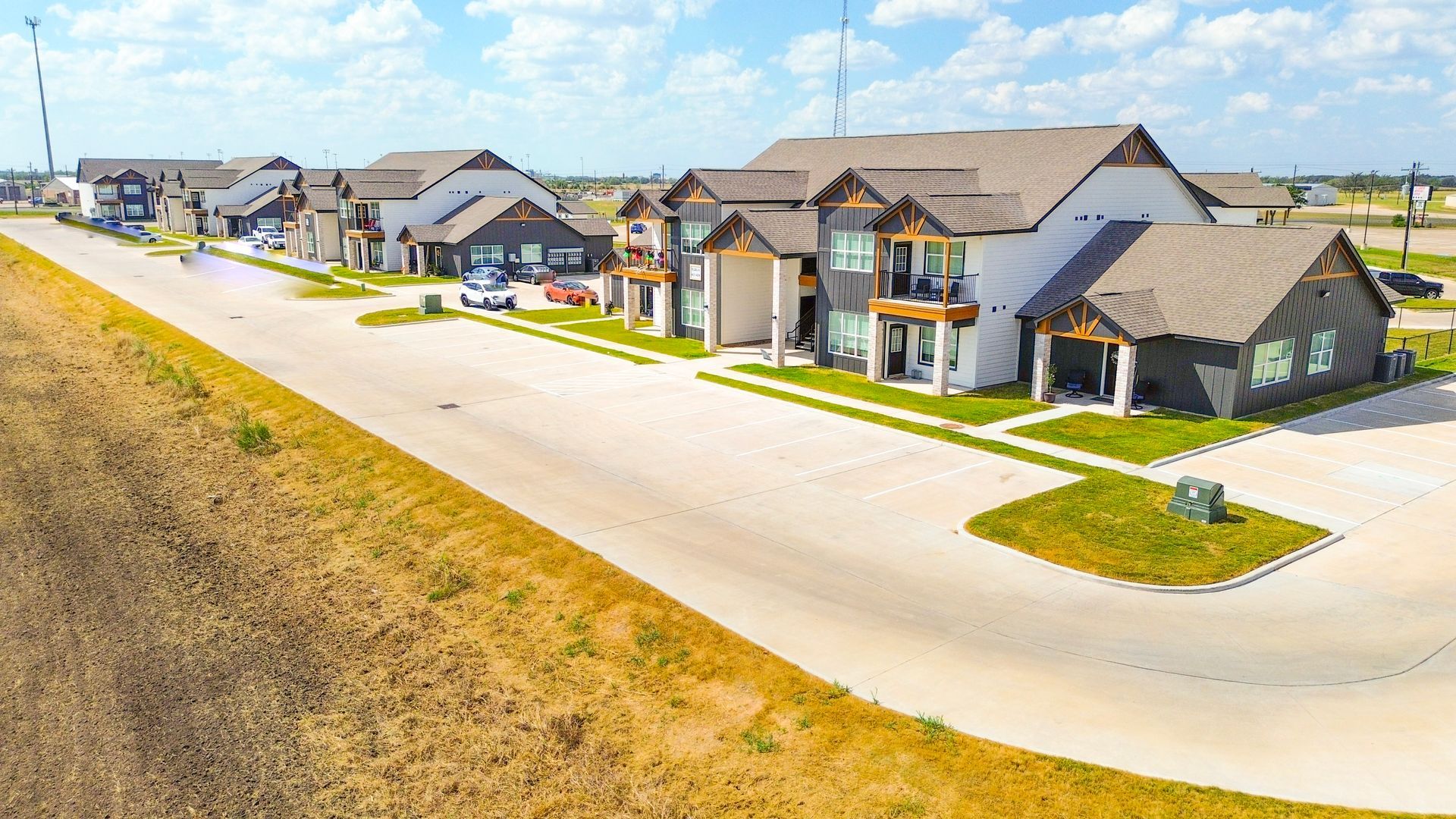 Residential buildings along a curved street under a blue sky, some with dark siding, others white.