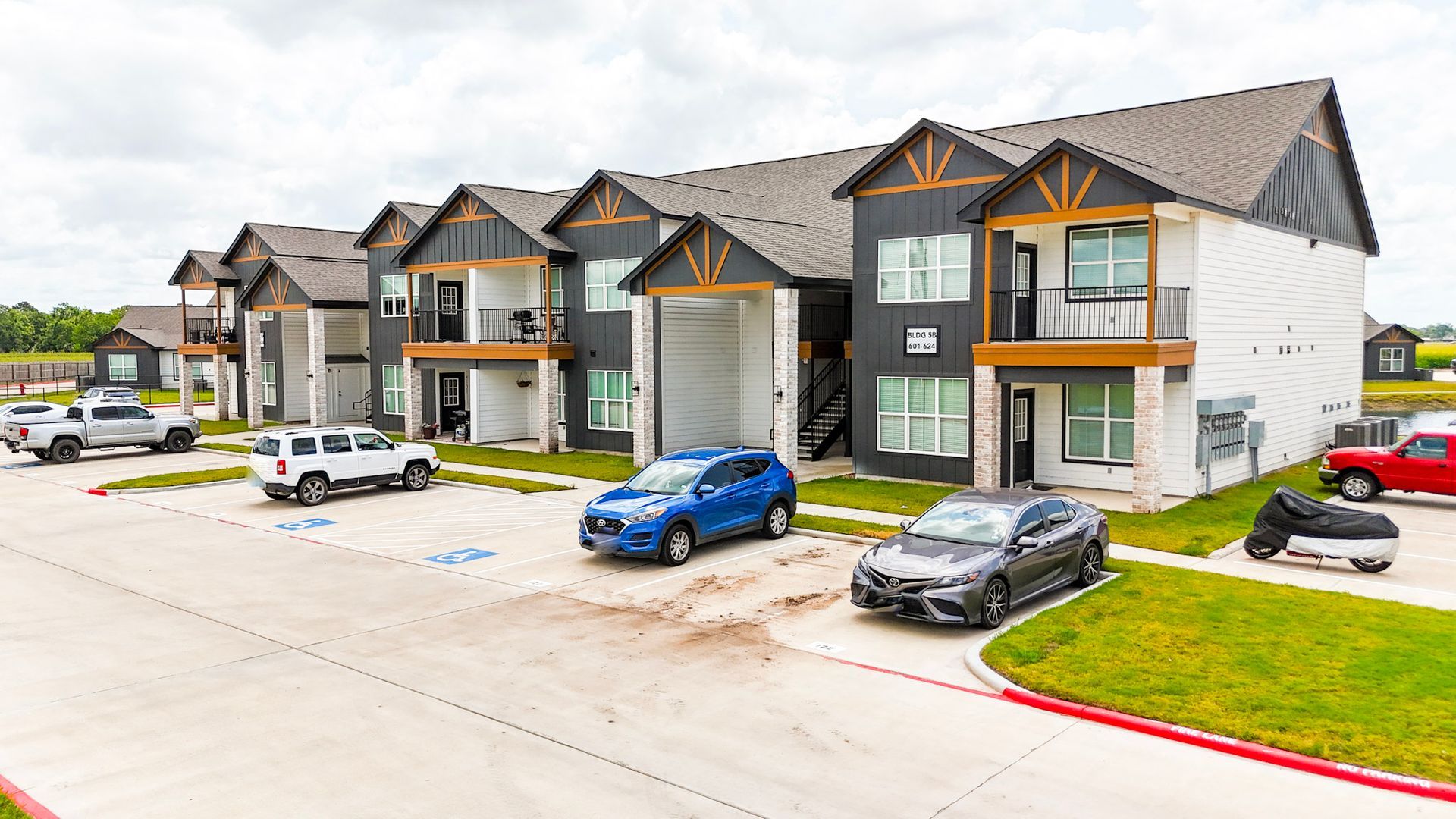 Apartment building with gray siding, brown roof, and parking lot on a sunny day.