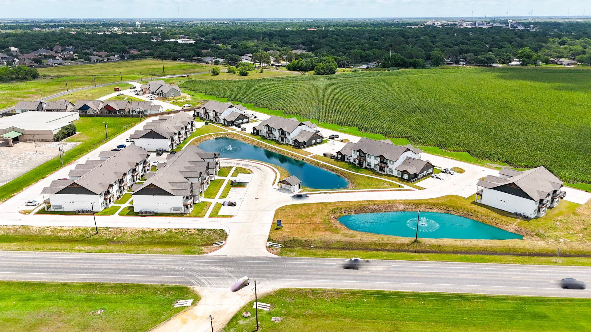 Rows of townhouses next to a pond under a bright blue sky with puffy clouds.