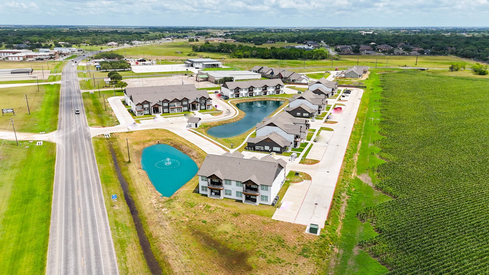 Aerial view of apartment buildings with brown roofs near a road and field.