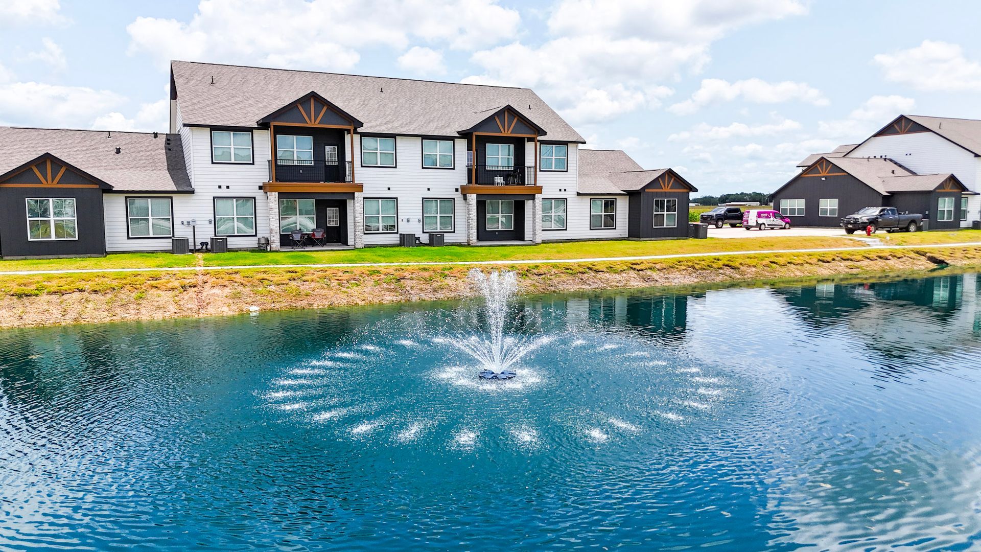Aerial view of buildings, roads, and green fields under a blue sky.