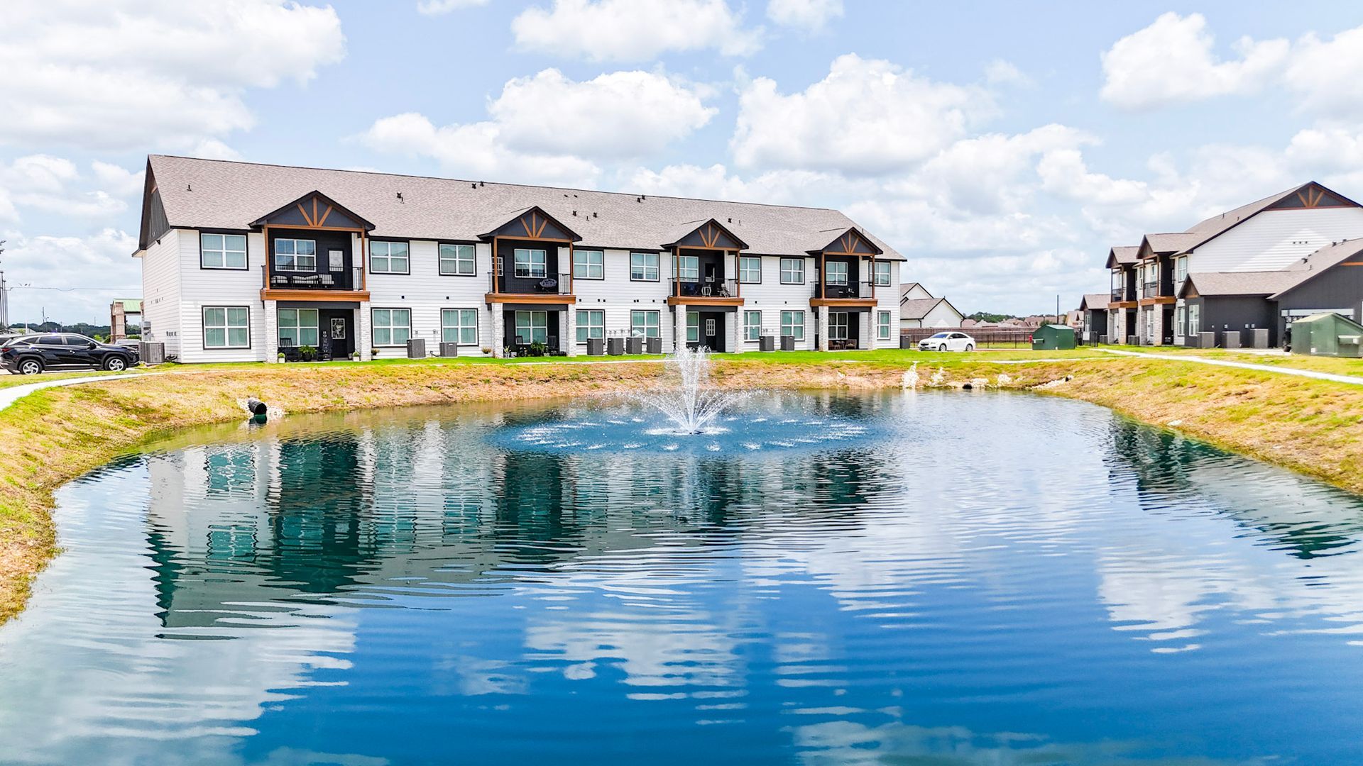 Aerial view of modern townhomes with light-colored siding, dark roofs, and manicured landscaping in a rural setting.