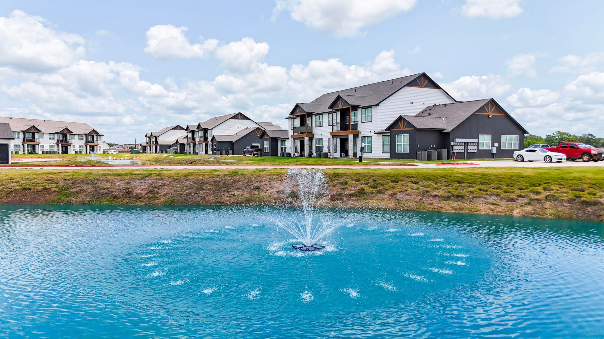 Residential buildings along a curved street under a blue sky, some with dark siding, others white.