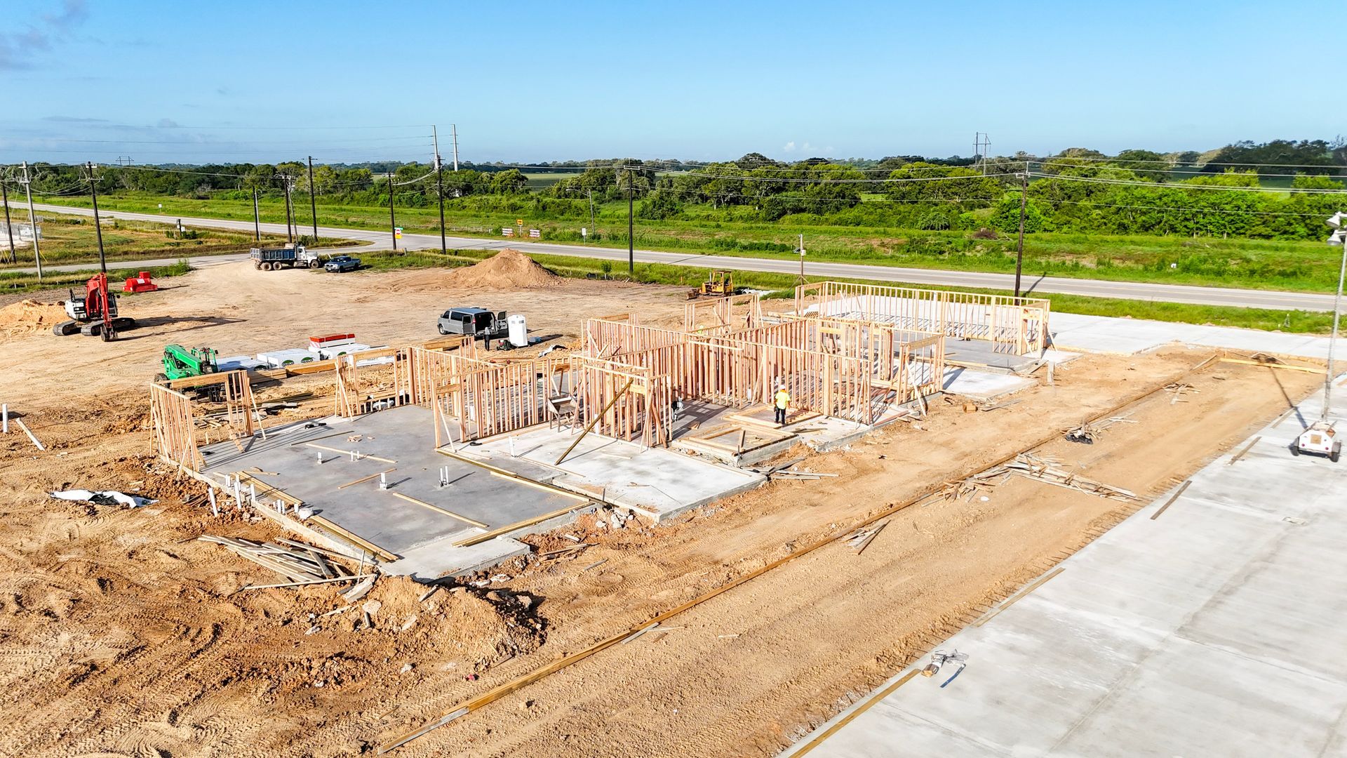 Construction site with wood framing for a house on a concrete foundation, dirt, and some construction equipment.