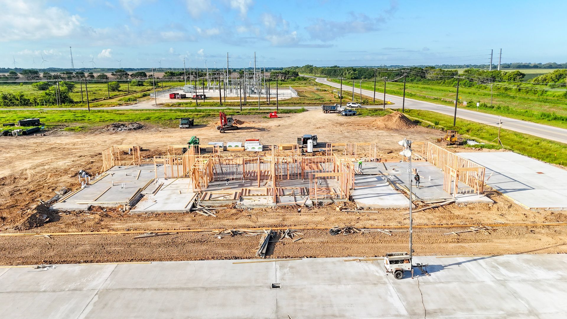Construction site with foundation framed; wind turbines in the background. Sunny day.