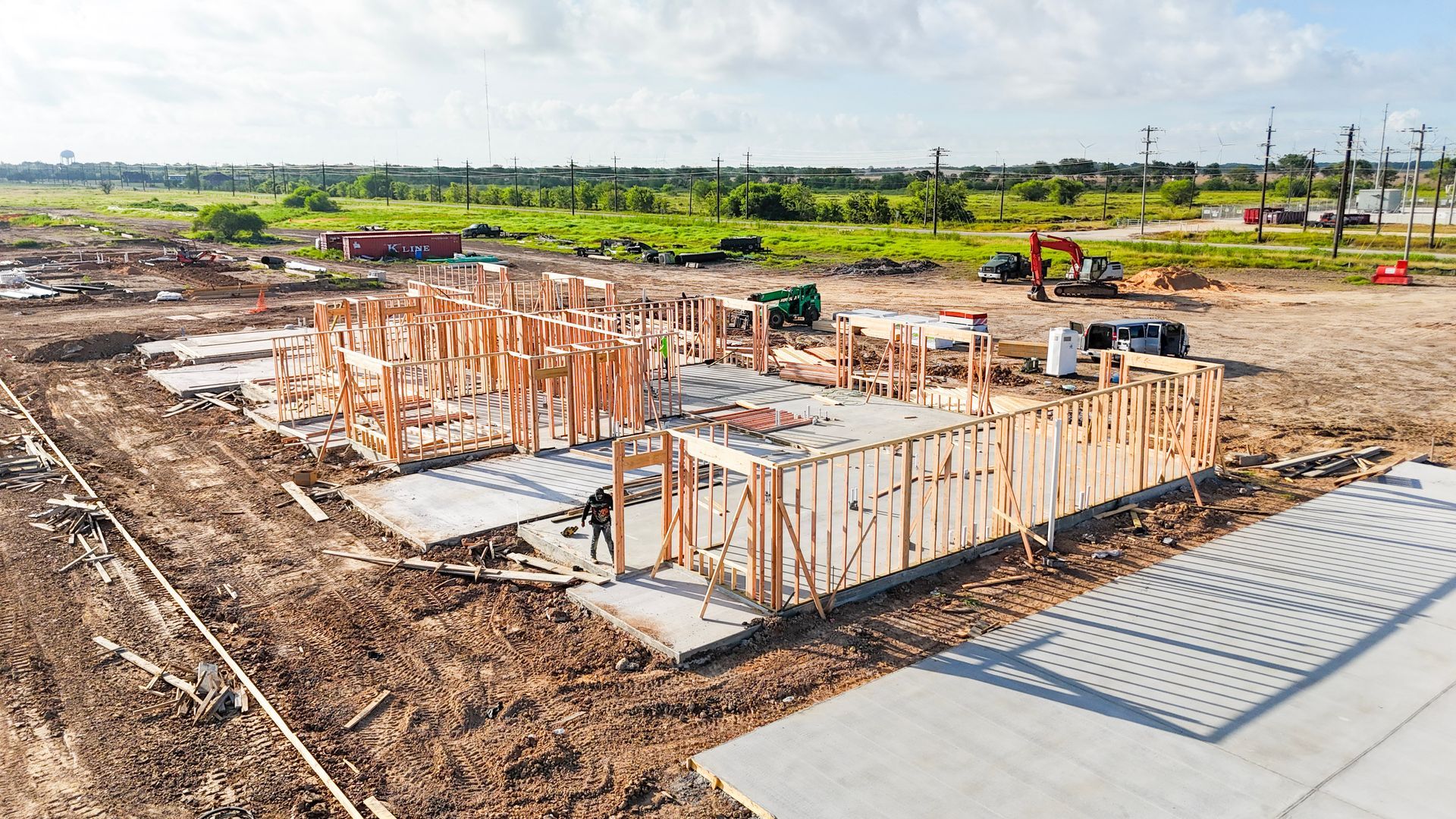 Construction site with wooden framework of a building on a concrete foundation, dirt surroundings.