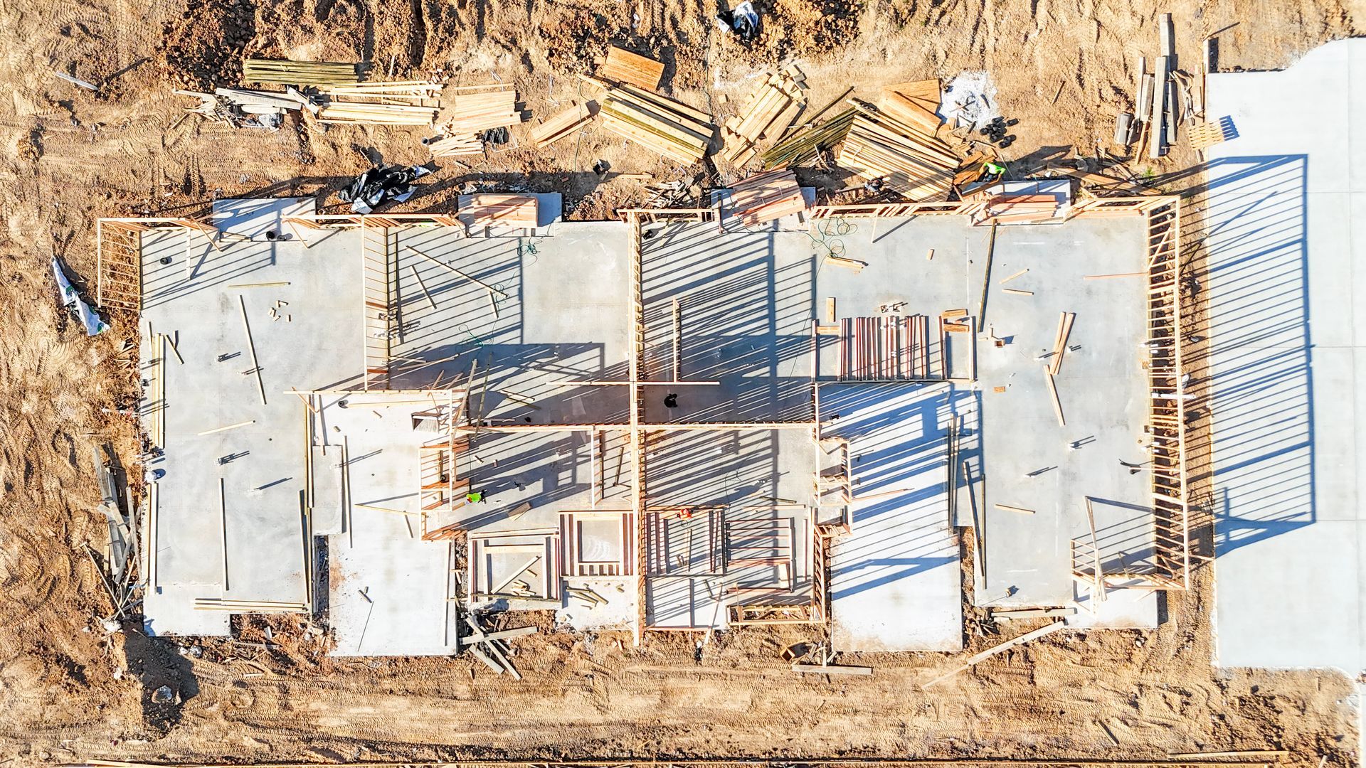Overhead view of a building under construction, showing concrete foundation and wooden framing on a dirt lot.
