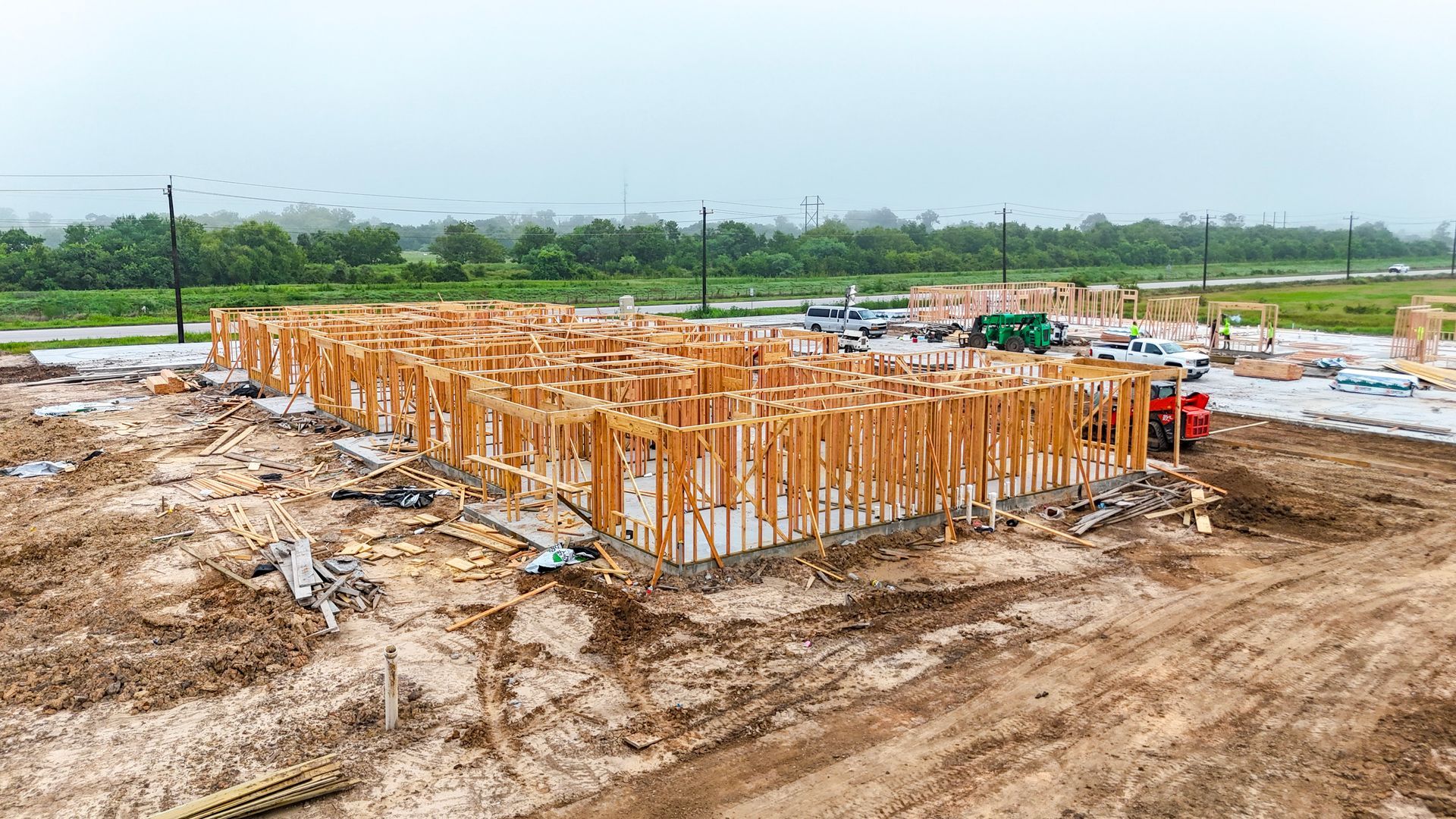 Wooden frame of a house under construction in a muddy field on an overcast day.