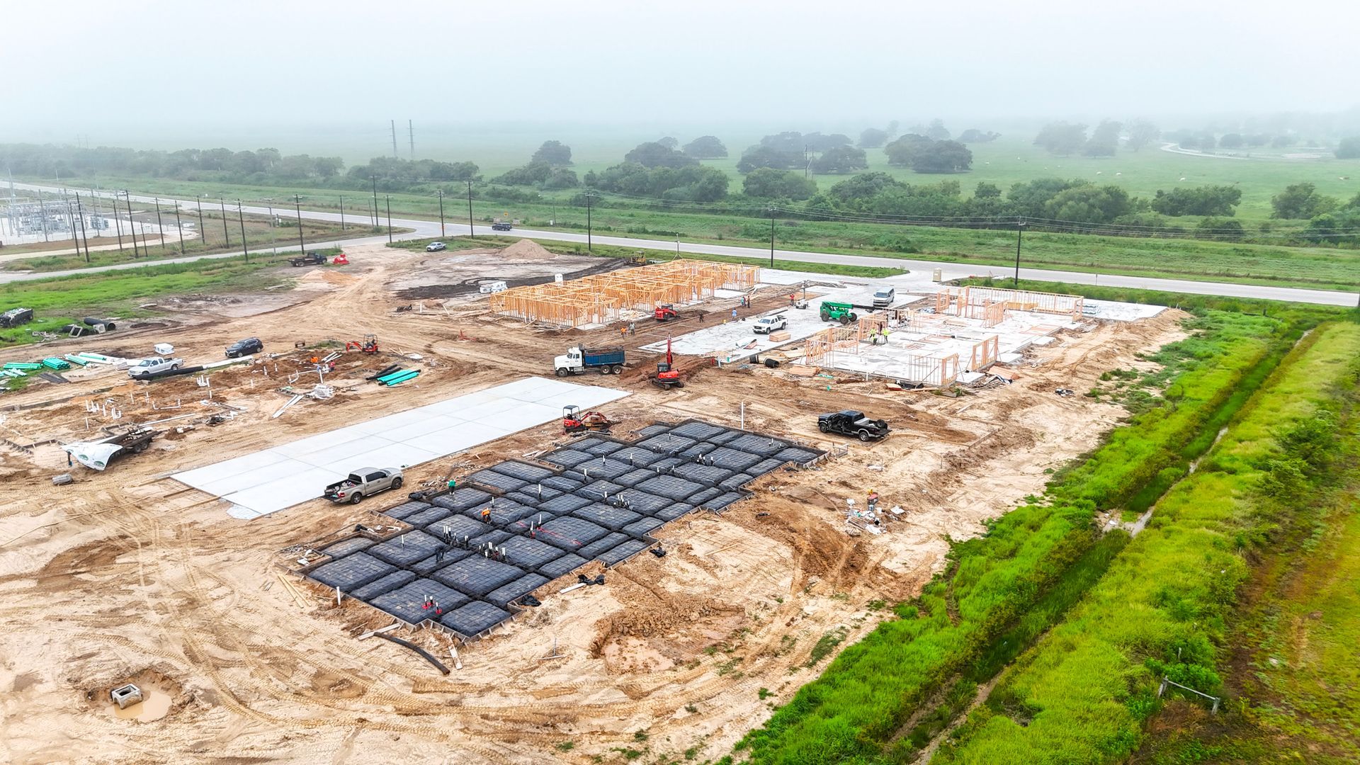 Construction site with dirt, foundations, and building framing on a cloudy day.