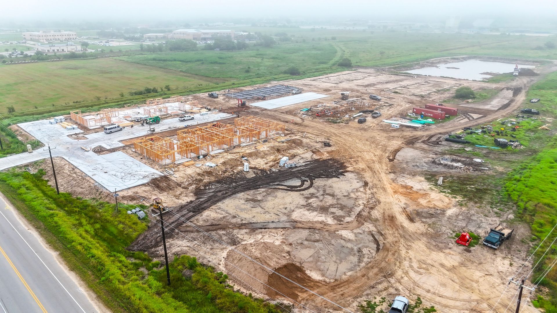 Aerial view of a construction site with building foundations, earth-moving equipment, and a road under construction.