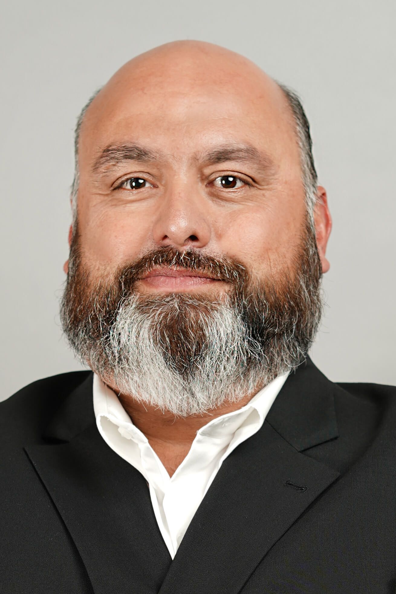 Man with a full beard wearing a suit jacket and white shirt, looking at the camera.