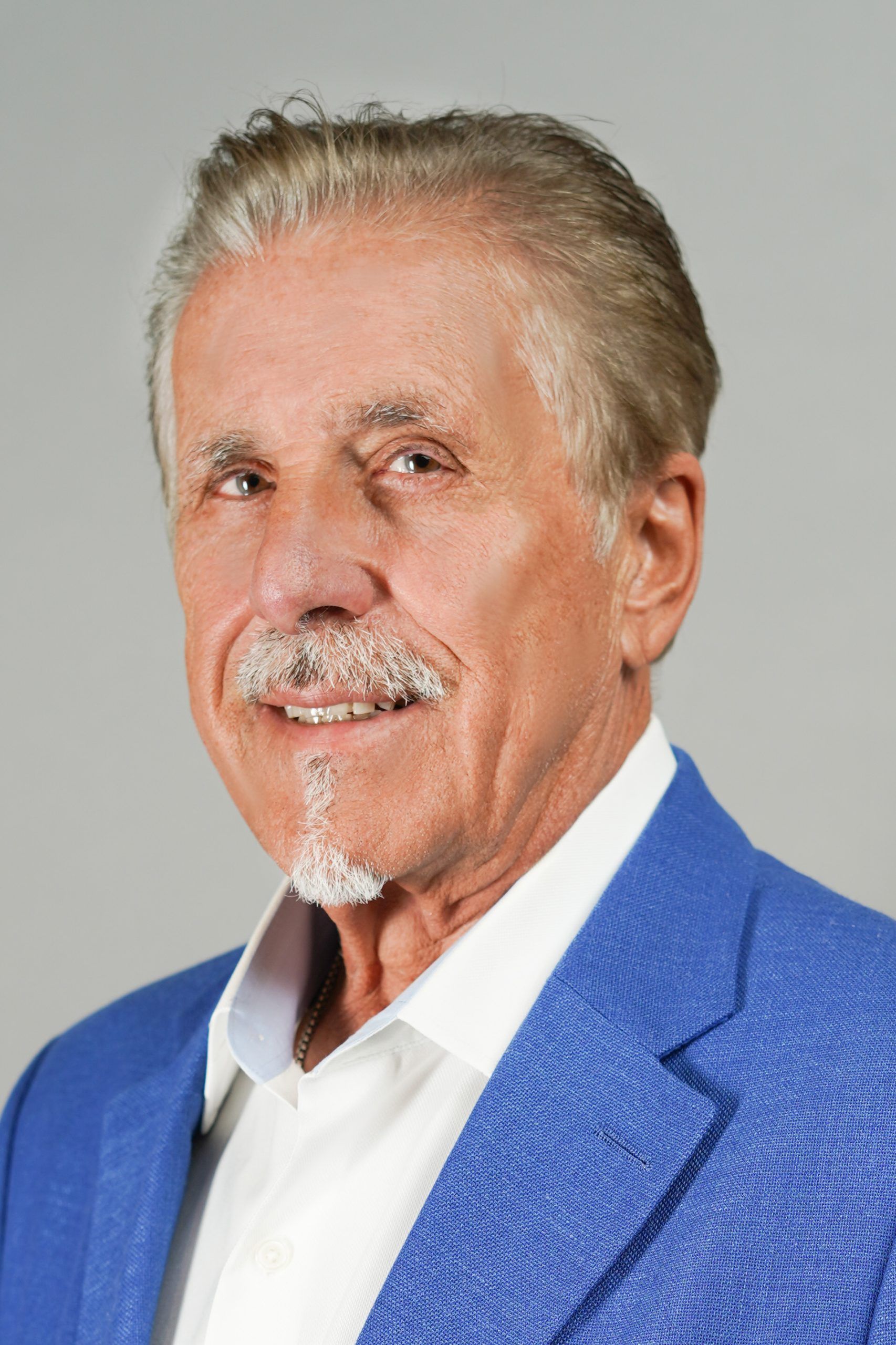 Man in a blue blazer smiles, with a goatee and white hair.