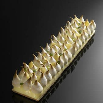 Un long morceau de gâteau avec de la meringue dessus sur une surface noire.